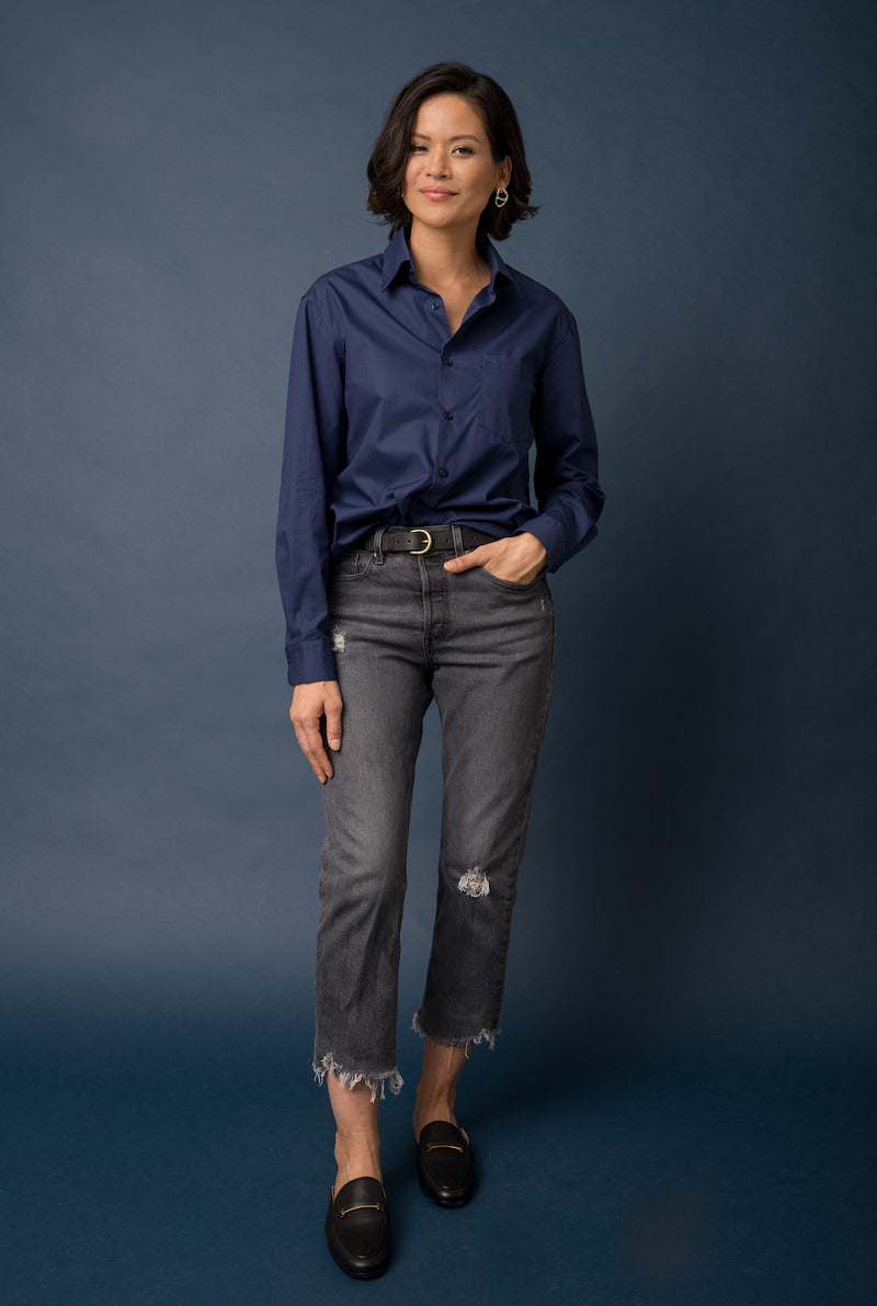 A woman wears a dress shirt that is inspired by a classic men’s button-down and has tucked it into her straight-fit jeans.