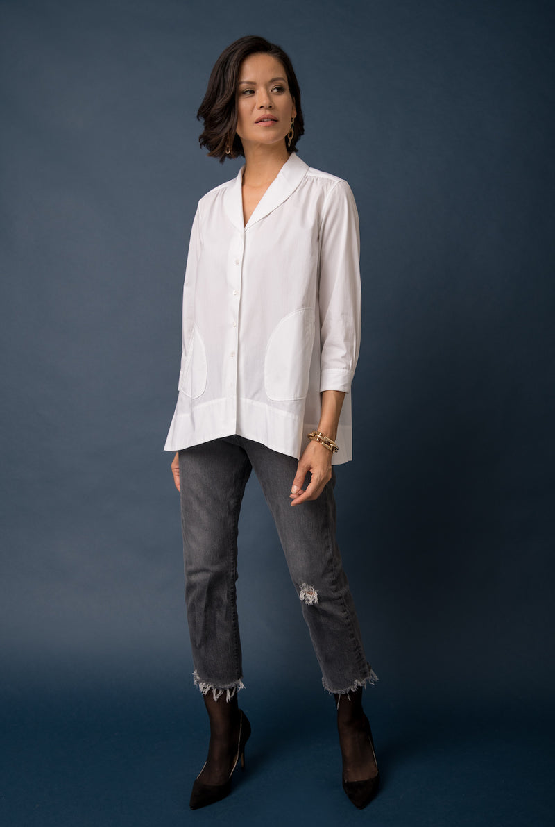 A woman wears a white tunic top with pockets that has an A-line silhouette and three-quarter sleeves.