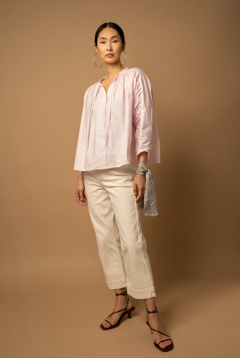 A woman wears a pink cotton peasant blouse that has three-quarter sleeves.