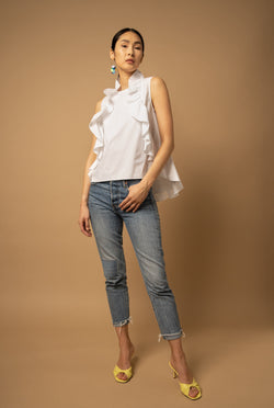 A woman wears a white ruffle top that has ruffles framing both sides of her chest.